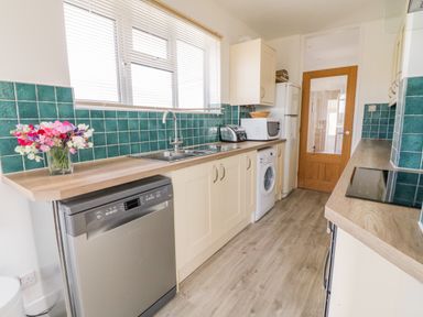 A kitchen with turquoise tile backsplash dishwasher washing machine microwave toaster and flowers on the counter at Senafe in Widemouth Bay