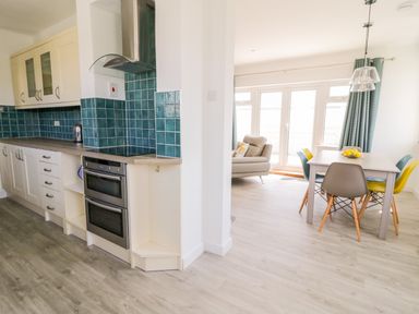 A kitchen with blue tiled backsplash adjacent to a dining area with a table and multicolored chairs at Senafe in Widemouth Bay