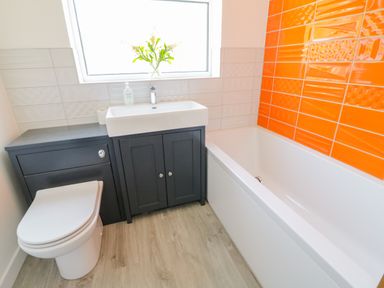 A bathroom with a toilet sink and bathtub with orange and white wall tiles at Senafe in Widemouth Bay