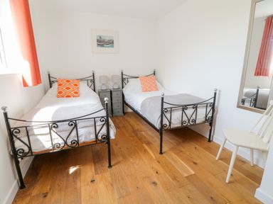 A bedroom with two single beds with orange pillows and a grey bedside table with lamps at Senafe in Widemouth Bay