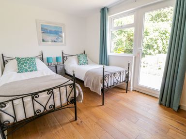 A bedroom with two single beds side by side blue pillows and lamps a window and door with curtains at Senafe in Widemouth Bay