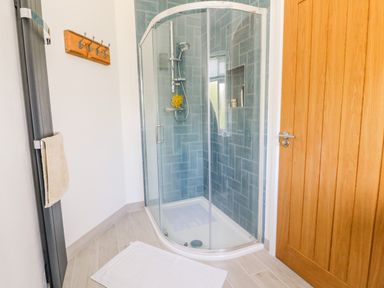 A bathroom with a curved glass shower enclosure wooden door towel rack and white bath mat at Senafe in Widemouth Bay