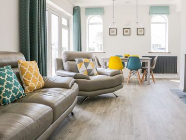 A living room with leather sofas and colorful cushions next to a dining table with mixed color chairs at Senafe in Widemouth Bay