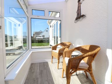 A sunroom with two wicker chairs and a small round table at Senafe in Widemouth Bay