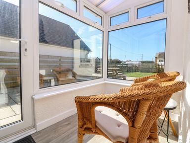 A sunroom with two wicker chairs and a small round table at Senafe in Widemouth Bay