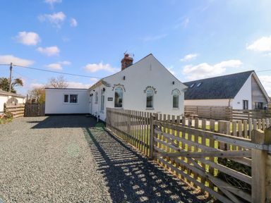 A white house with a gravel driveway and wooden fence under a blue sky at Senafe in Widemouth Bay