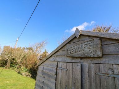 A wooden shed with a sign that reads Senafe in a grassy garden with trees at Senafe in Widemouth Bay