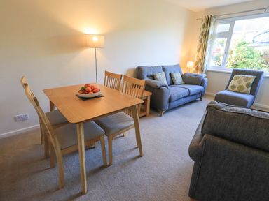 A living room with a wooden dining table and chairs a bowl of fruit two sofas an armchair a floor lamp and a window at Fairfell in Keswick