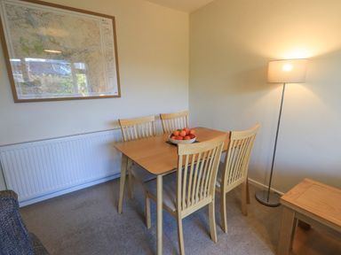A dining area with a wooden table and four chairs a bowl of fruit on the table a floor lamp and a framed map on the wall at Fairfell in Keswick