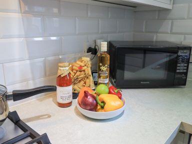 A kitchen countertop with a pot on a stove pasta sauce bottle a bag of pasta rapeseed oil microwave and a bowl of vegetables including onions and peppers at Fairfell in Keswick