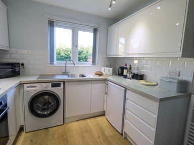 A kitchen with white cabinets a washing machine a refrigerator microwave and a window at Fairfell in Keswick