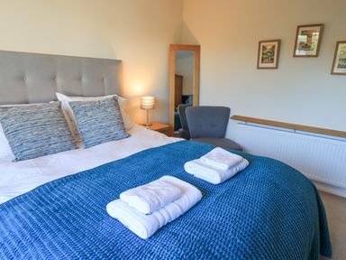 A bedroom with a bed with blue bedding and folded towels and a chair and a standing mirror at Fairfell in Keswick