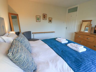 A bedroom with a bed with blue pillows and blanket a chair a wooden dresser with a mirror and a floor mirror at Fairfell in Keswick