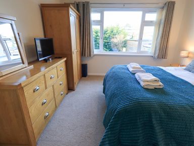 A bedroom with a bed covered in a blue blanket and towels on top a wooden dresser with a TV and a wooden wardrobe next to a large window at Fairfell in Keswick