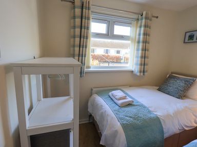 A bedroom with a single bed next to a window with plaid curtains and a small white shelving unit at Fairfell in Keswick