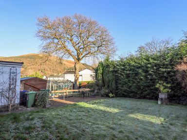 A garden with a large tree a greenhouse outdoor chairs and table and a hedge at Fairfell in Keswick