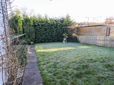 A backyard with a concrete path along the left side grass and hedge fencing at Fairfell Keswick