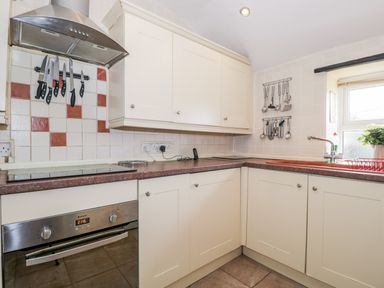 A kitchen with white cabinets a stainless steel oven and knives on a magnetic strip at Combe Cottage in Brimscombe near Stroud