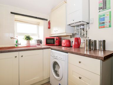 A kitchen with a washing machine red microwave toaster and kettle and metal canisters on the counter at Combe Cottage in Brimscombe near Stroud