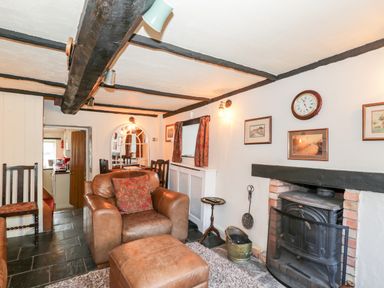 A living room with a leather armchair and ottoman near a fireplace with a wood stove at Combe Cottage in Brimscombe near Stroud