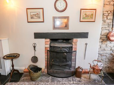 A fireplace with a wood stove and a protective screen surrounded by fireplace tools and decorative items at Combe Cottage in Brimscombe near Stroud