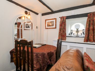 A dining area with wooden chairs a table covered with a patterned cloth and a mirror on the wall at Combe Cottage Brimscombe near Stroud