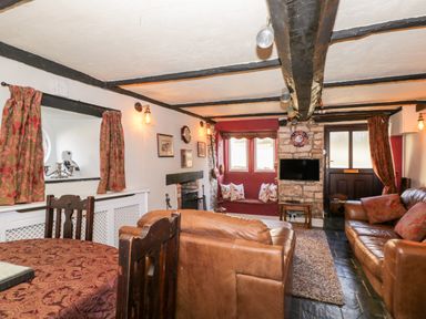 A living room with brown leather sofas a wooden dining table a fireplace and a wall-mounted television at Combe Cottage in Brimscombe near Stroud