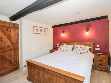 A bedroom with a wooden bed and bedside tables against a red accent wall at Combe Cottage Brimscombe near Stroud