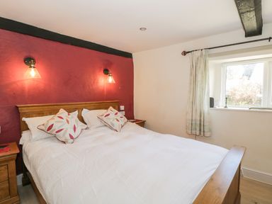 A bedroom with a wooden bed frame and white bedding against a red and white wall at Combe Cottage in Brimscombe near Stroud