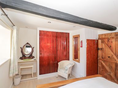 A bedroom with a wooden door a wicker chair a vanity table with a mirror and a window at Combe Cottage in Brimscombe near Stroud