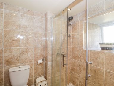 A bathroom with a toilet a glass shower enclosure and beige tiled walls at Combe Cottage Brimscombe near Stroud