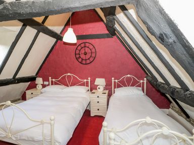 A bedroom with two beds a bedside table and a clock on the wall at Combe Cottage in Brimscombe near Stroud
