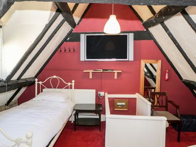 A bedroom with a single bed a small table a wall-mounted TV a mirror and a wooden chair at Combe Cottage Brimscombe near Stroud