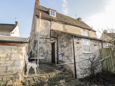 Exterior view of a stone cottage with a small patio area containing two white chairs and a table at Combe Cottage in Brimscombe near Stroud