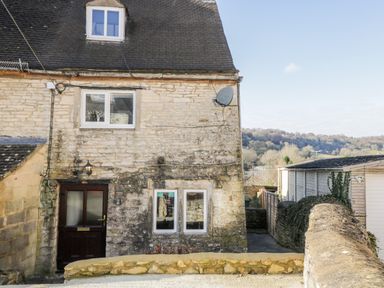 Stone exterior of a house with windows and a door and a satellite dish at Combe Cottage in Brimscombe near Stroud
