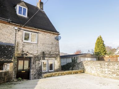 The exterior of a stone house with a wooden door driveway and a stone wall at Combe Cottage in Brimscombe near Stroud