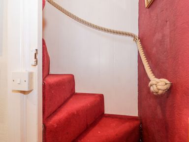A staircase with red carpet and a twisted rope handrail at Combe Cottage in Brimscombe near Stroud