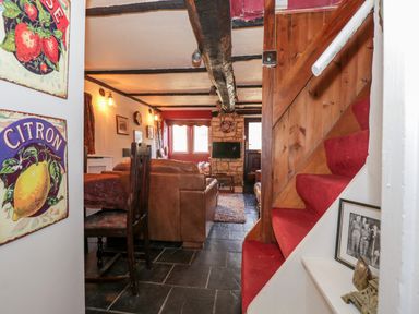 A living room with a brown sofa wooden staircase with red carpet and citrus fruit wall signs at Combe Cottage Brimscombe near Stroud
