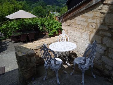 An outdoor seating area with a white metal table and three chairs beside a stone wall at Combe Cottage in Brimscombe near Stroud