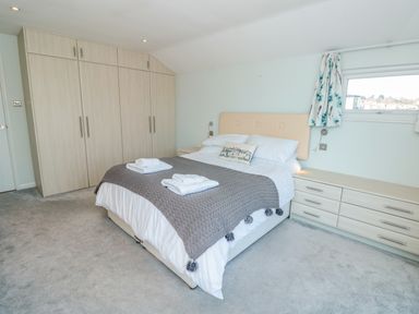 A bedroom with a double bed, wardrobe, chest of drawers, and a window with curtains at Estuary View House and Annexe in Dartmouth