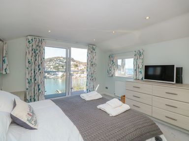 A bedroom with a bed towels dresser and a television with a view of water and hills at Estuary View House and Annexe in Dartmouth