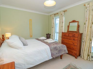 A bedroom with a bed a wooden dresser with mirror and floral curtains at Estuary View House and Annexe Dartmouth