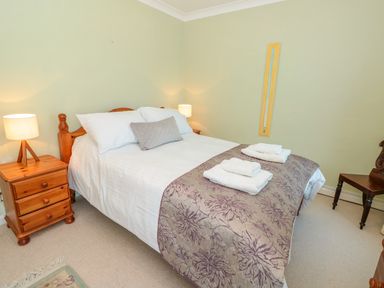 A bedroom with a double bed bedside tables lamps a chair and folded towels at Estuary View House Annexe in Dartmouth