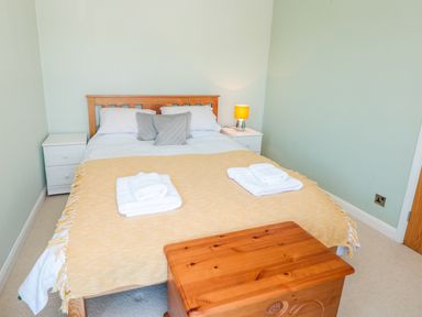 A bedroom with a wooden bed frame white bedding yellow blanket two bedside tables with lamp and folded towels at Estuary View House and Annexe in Dartmouth