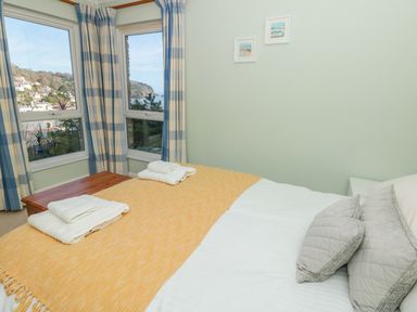 A bedroom with a bed covered by a yellow blanket and folded towels near windows with striped curtains at Estuary View House and Annexe in Dartmouth