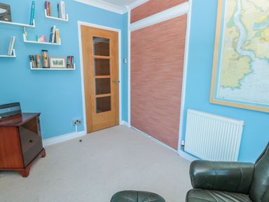 A room with light blue walls a door with glass panels shelves with books a framed map radiator and a leather chair at Estuary View House and Annexe in Dartmouth