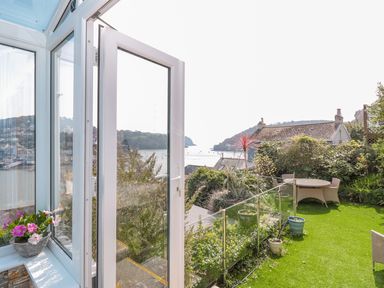 A garden area with a round table and chairs overlooking water and hills at Estuary View House and Annexe in Dartmouth