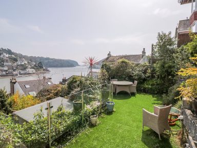 A garden with outdoor seating and potted plants overlooking a river and houses at Estuary View House and Annexe in Dartmouth