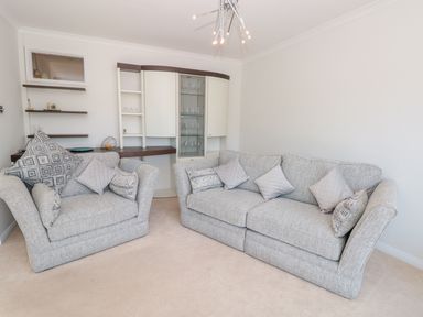 A living room with two grey sofas and cushions near shelves and a cabinet at Estuary View House and Annexe in Dartmouth