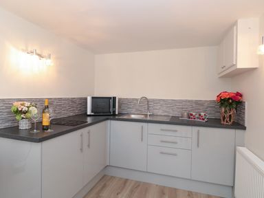 A kitchen with a microwave a sink wine glasses flowers and mugs at Estuary View House and Annexe in Dartmouth